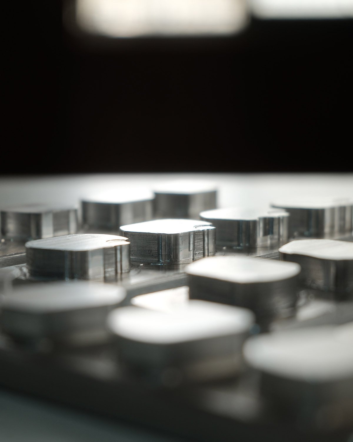 Rows of machined metal parts catching the light on a workbench, in black and white