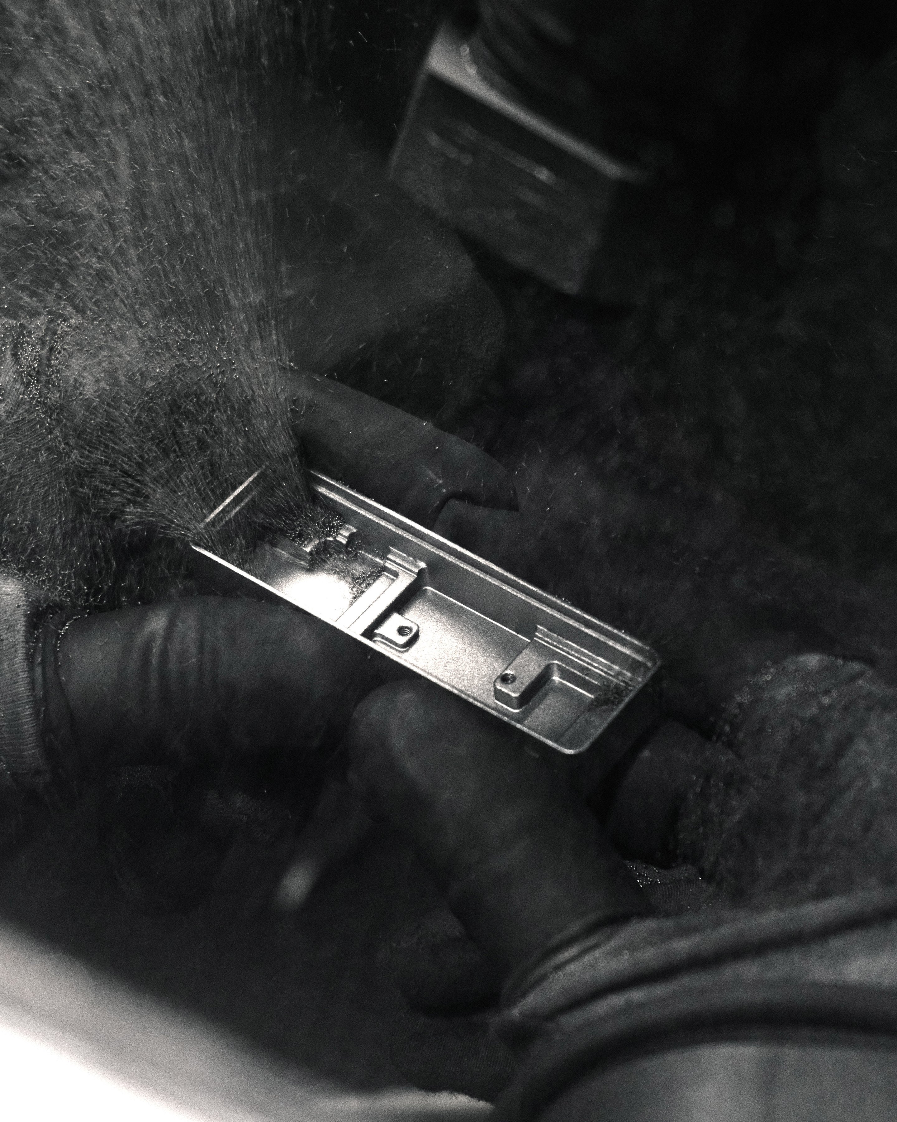Hands in work gloves polishing a small metal component, dust in the air, in black and white
