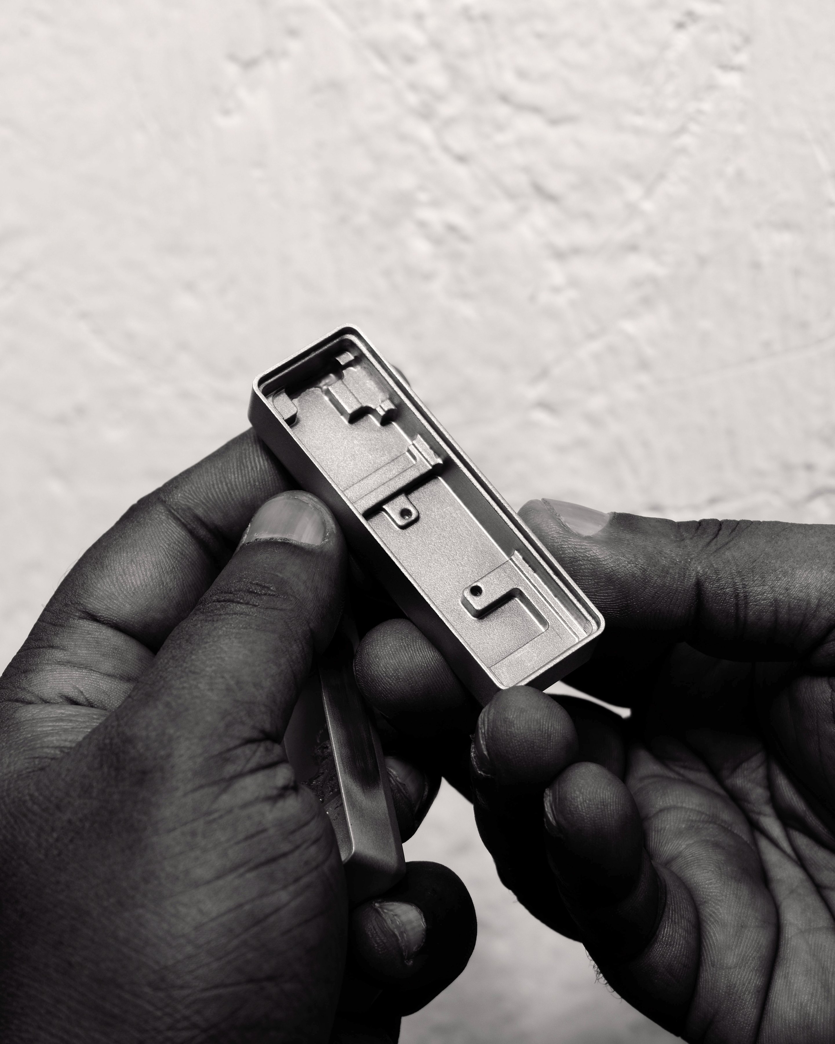 Hands holding a machined aluminium housing against a rough white wall, in black and white