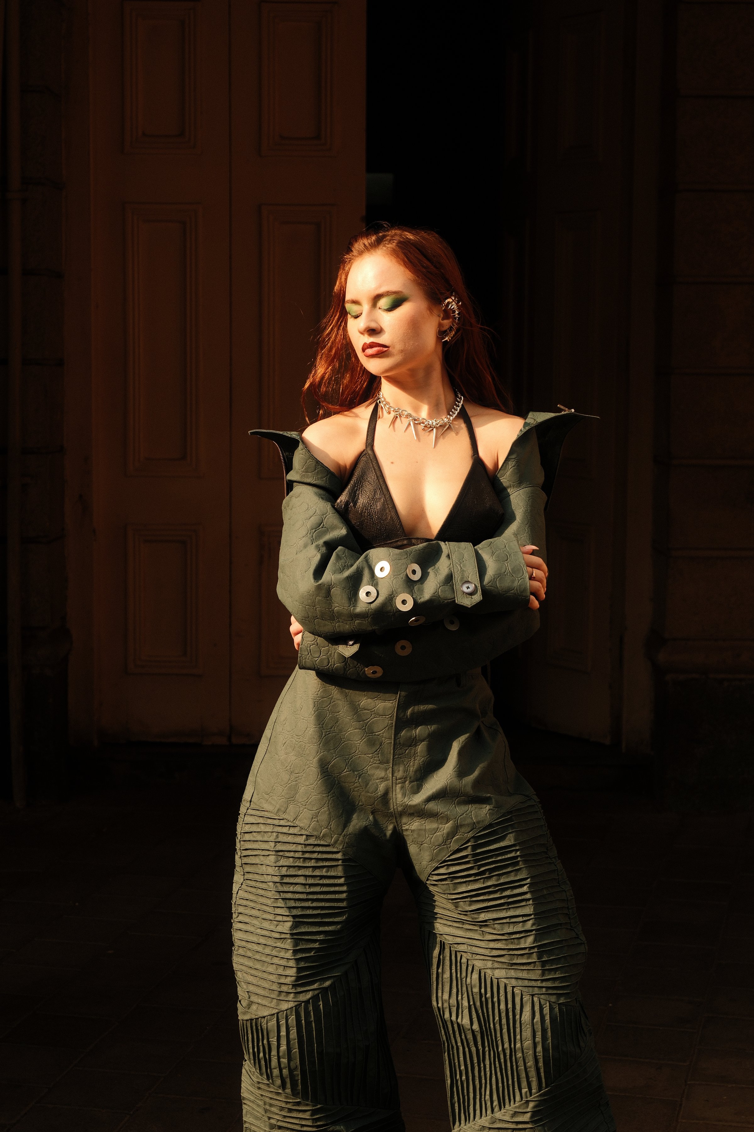 A model with arms crossed standing in a dark wooden doorway