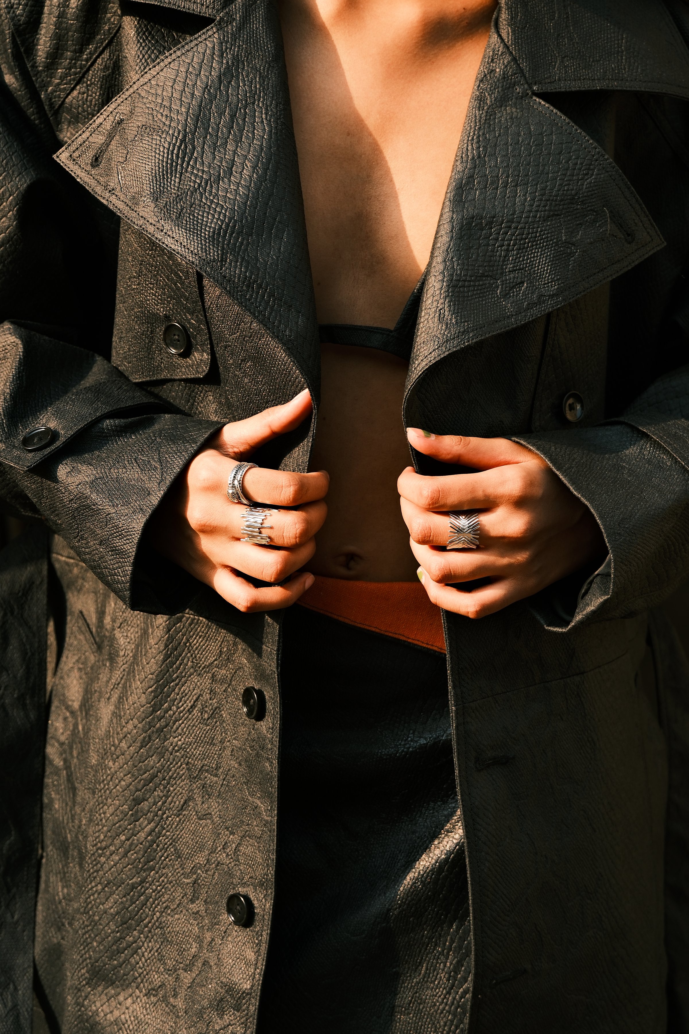 Hands with silver rings holding open a dark leather trench coat