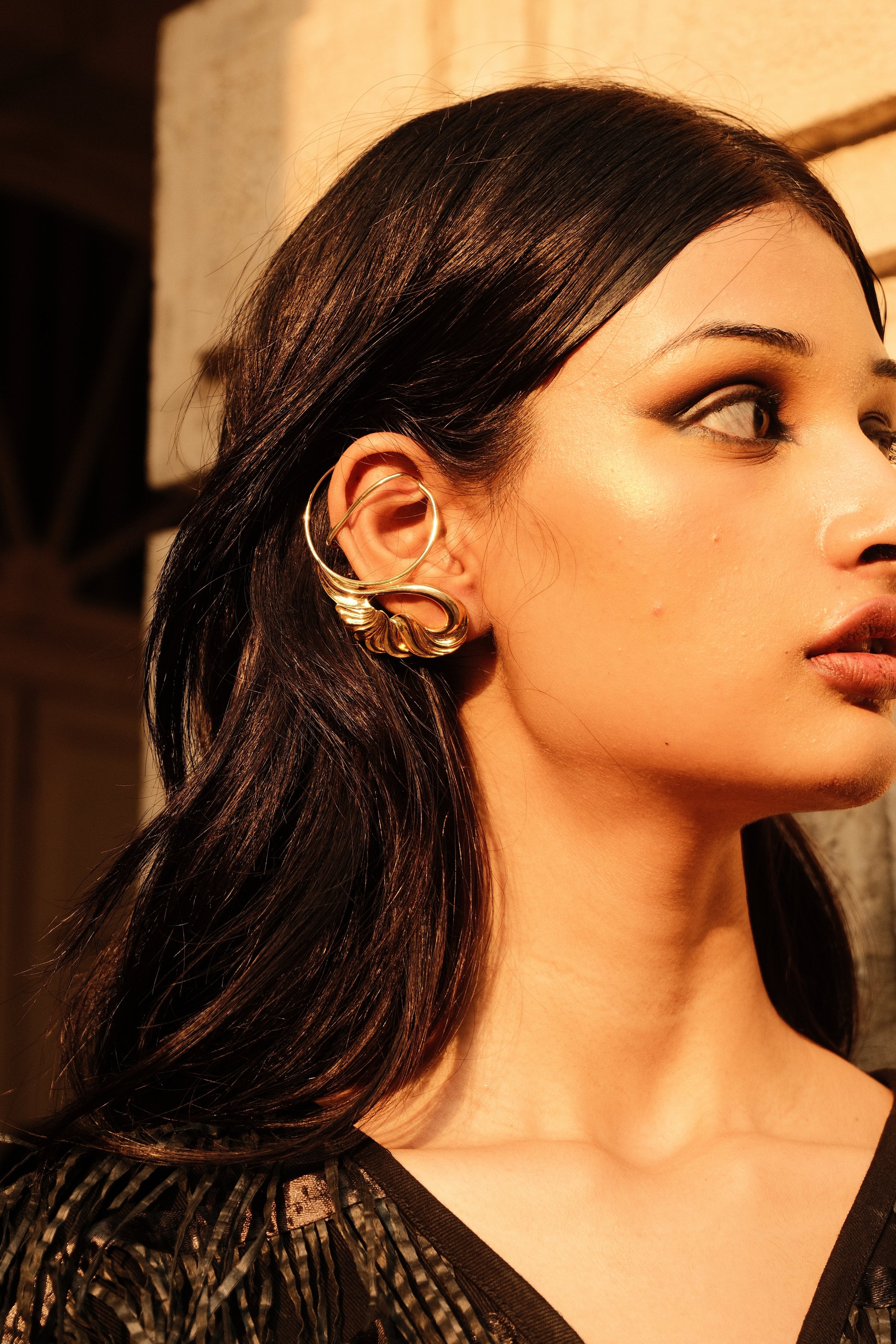 Close profile portrait of a model wearing a gold ear cuff