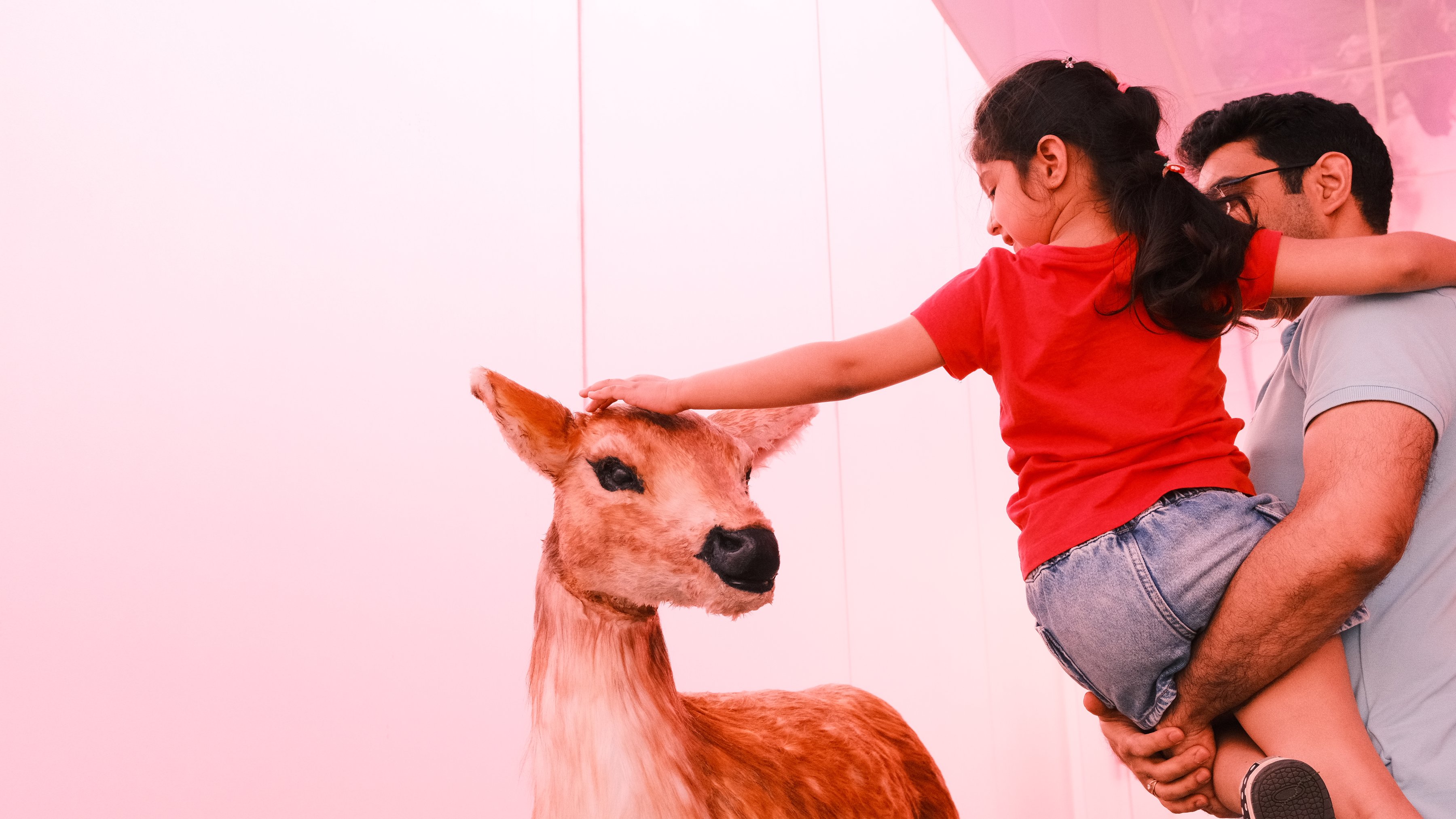 A father lifting his daughter to reach a fawn sculpture