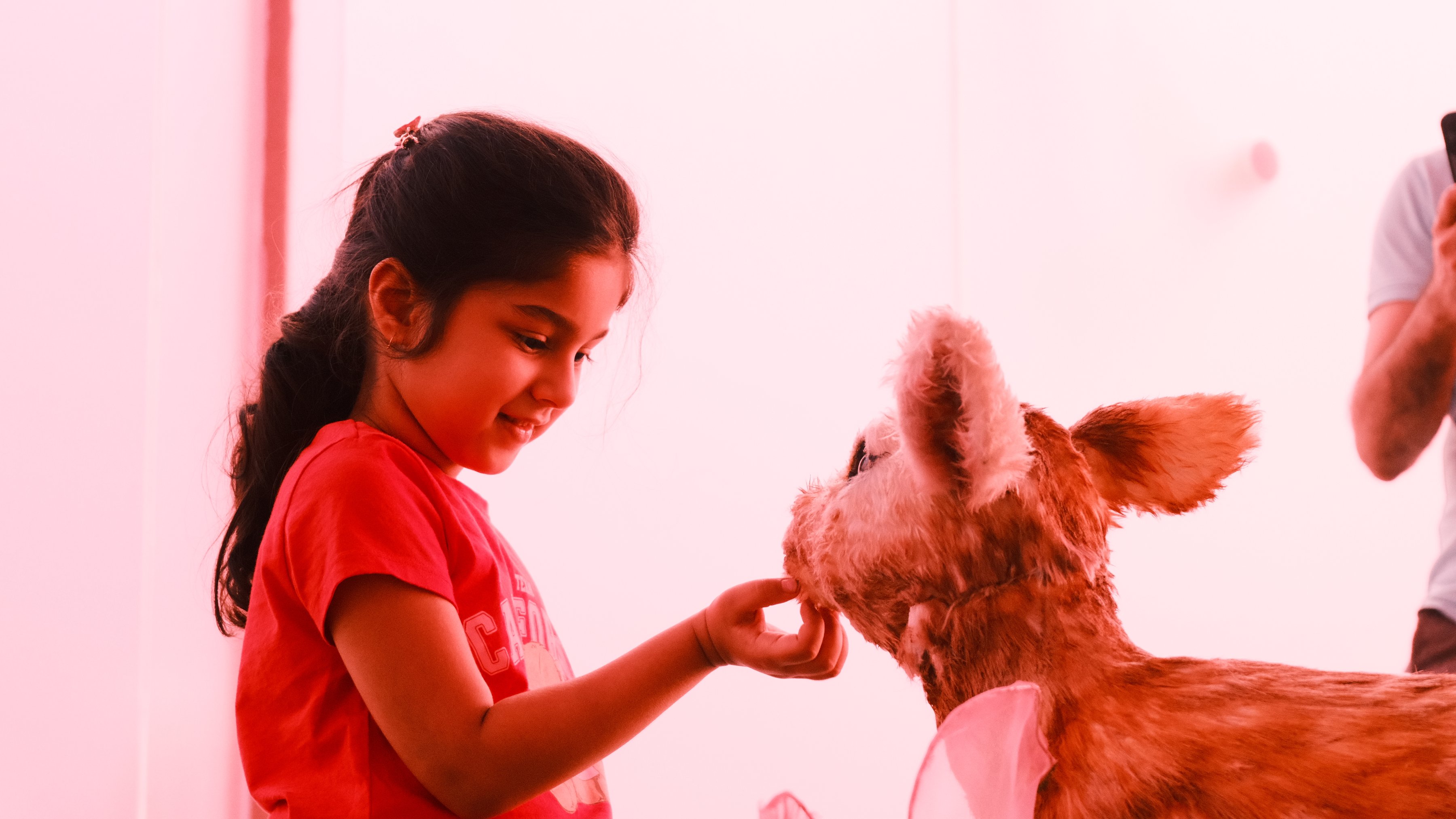 A girl in red holding her hand out to a fawn sculpture