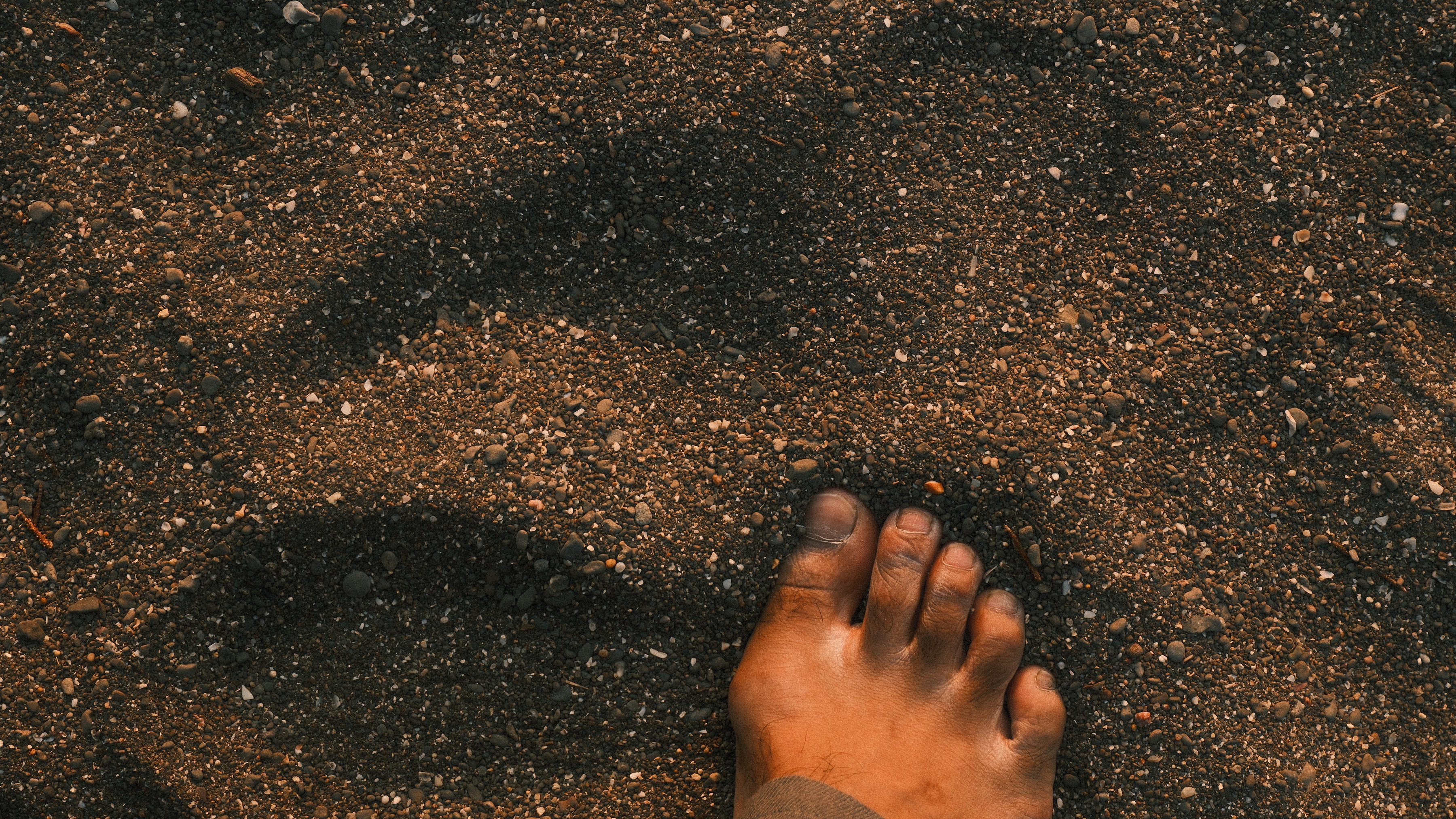 A bare foot pressing into dark sand