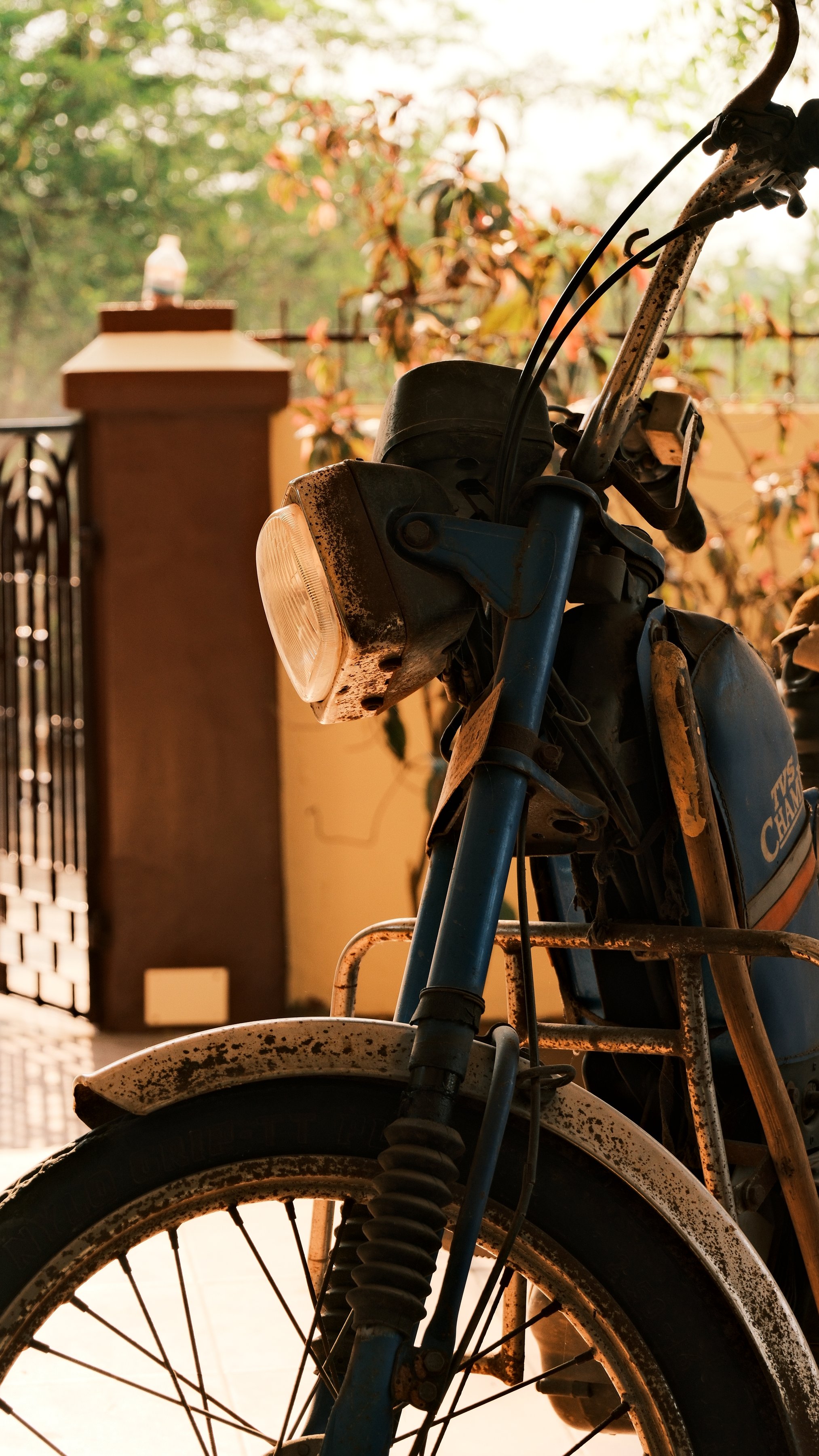 An old motorcycle parked by a gate in afternoon light