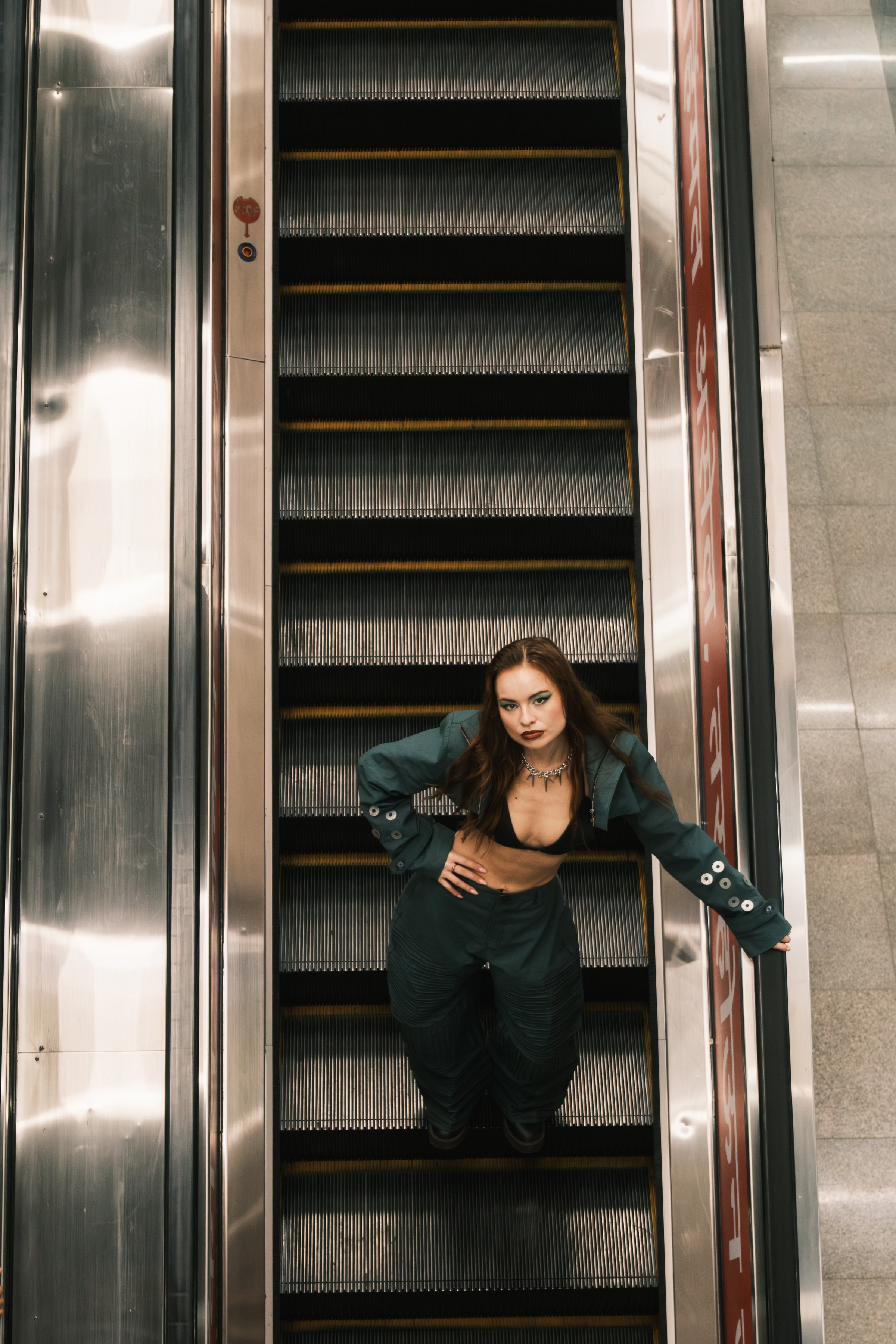 A model leaning on the escalator handrail, looking up at the camera