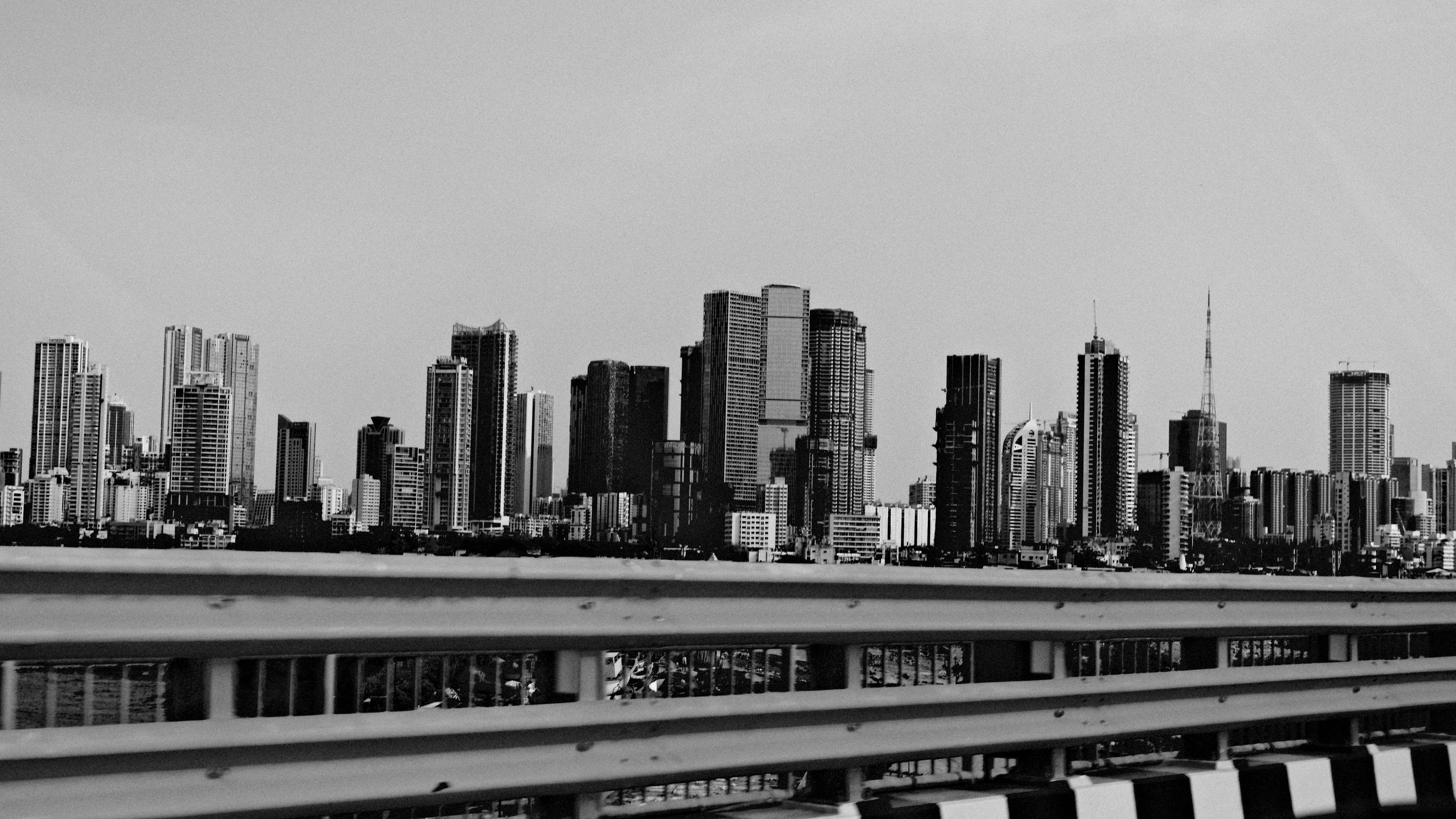 Tall towers above a railing by the water, in black and white