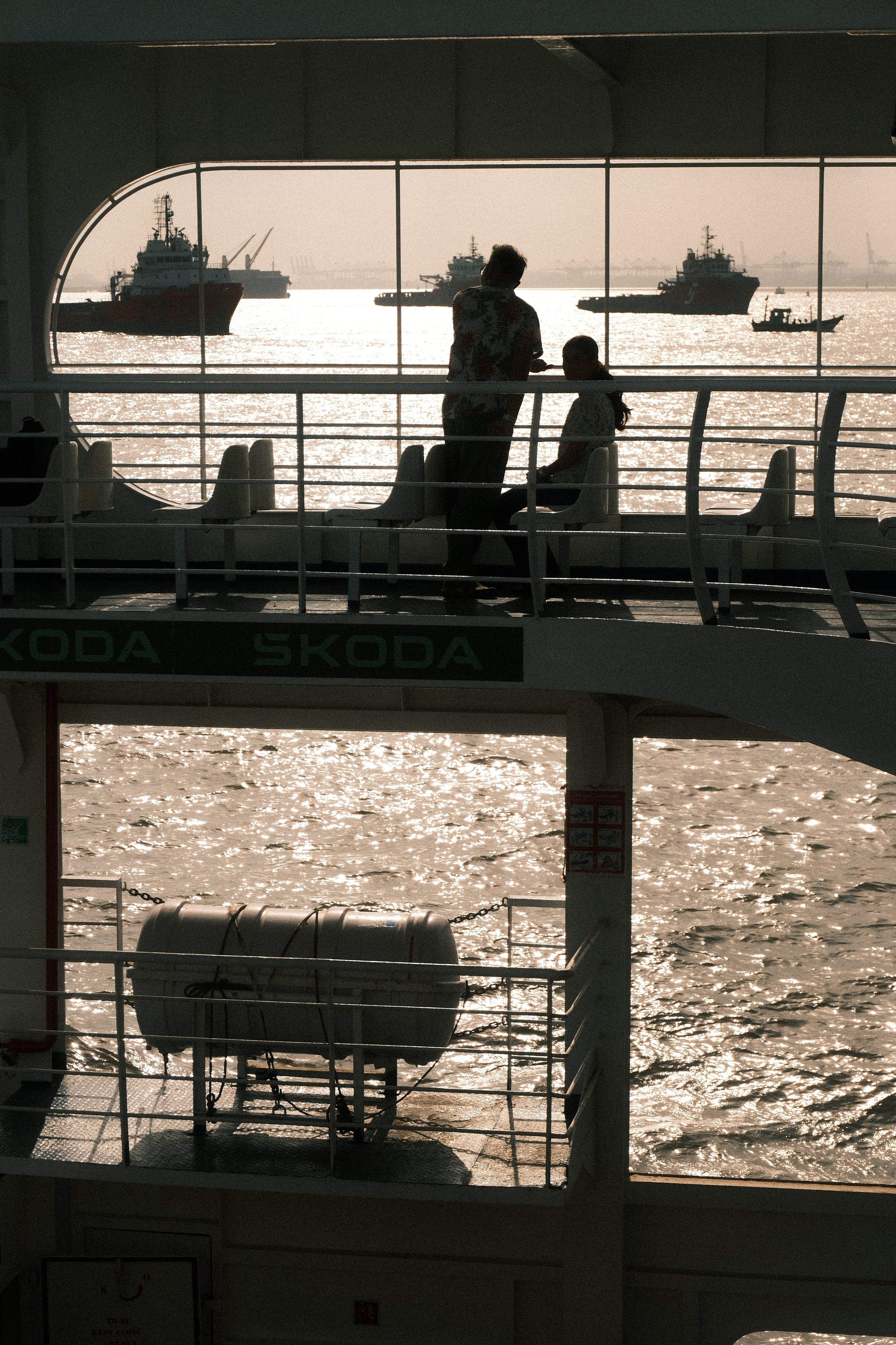 Figures on the upper deck of a ferry against a bright sea