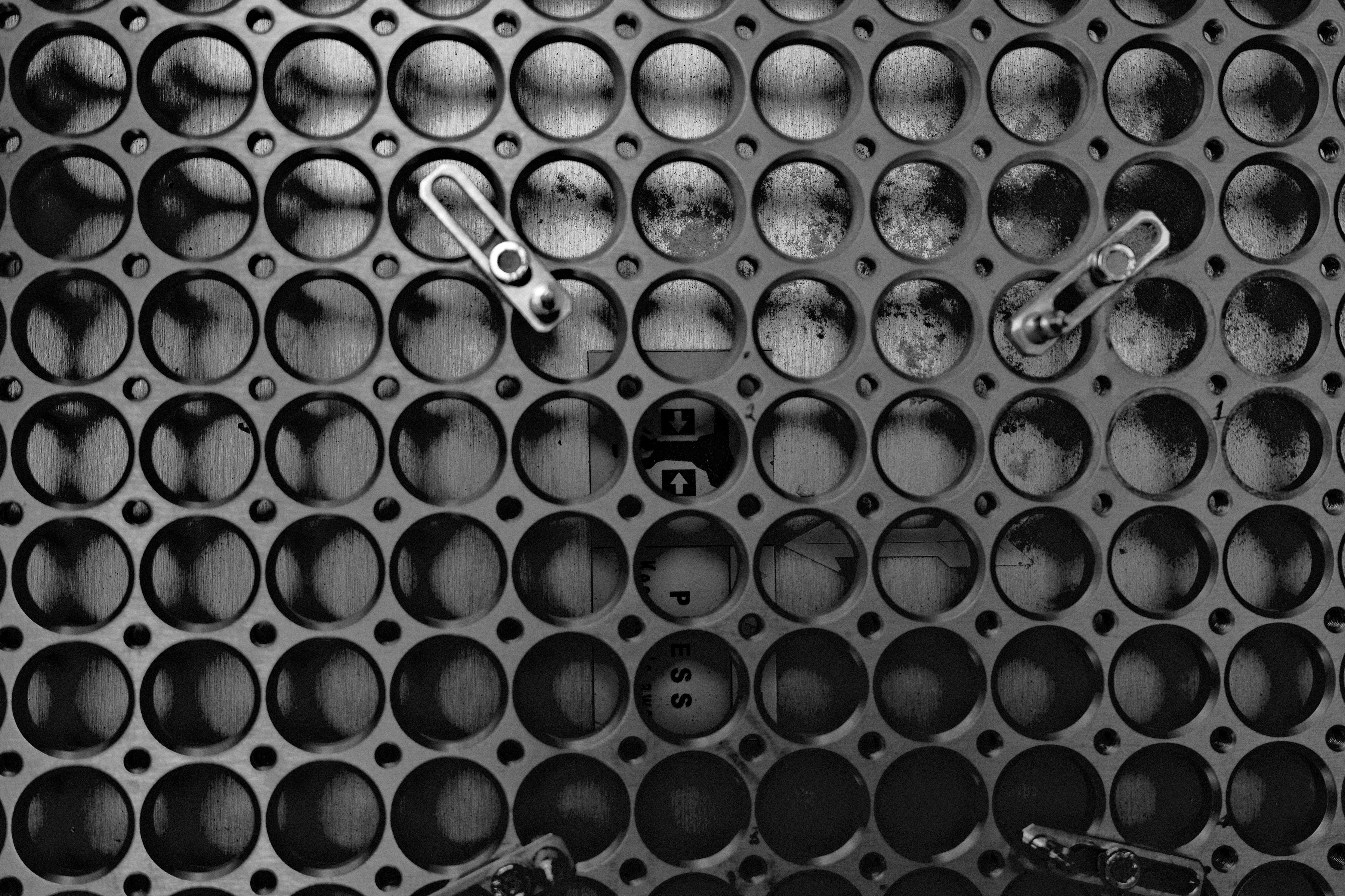 A wall of round metal holes with two small hooks, in black and white