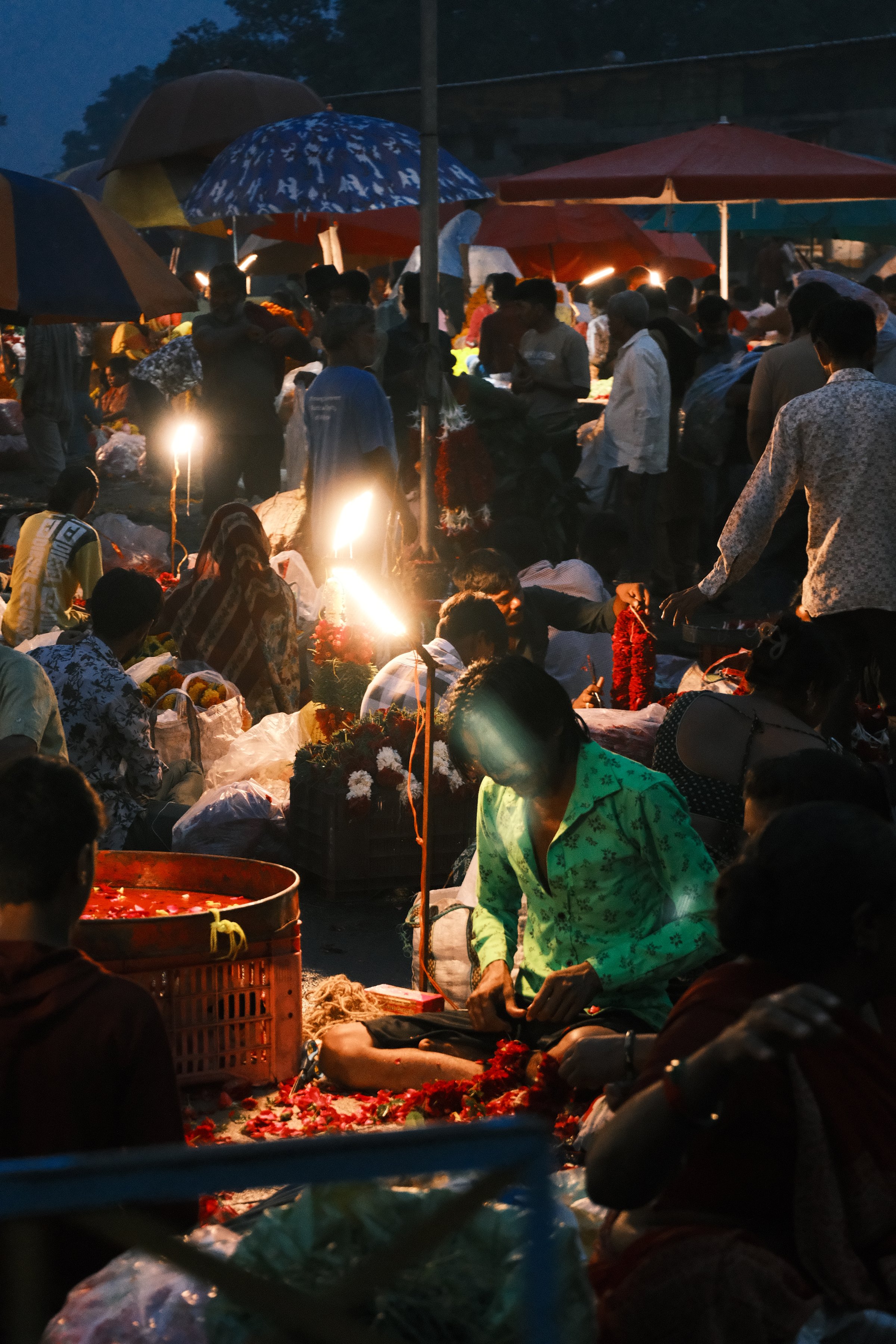 A man in a green shirt working through a pile of flowers by lamplight