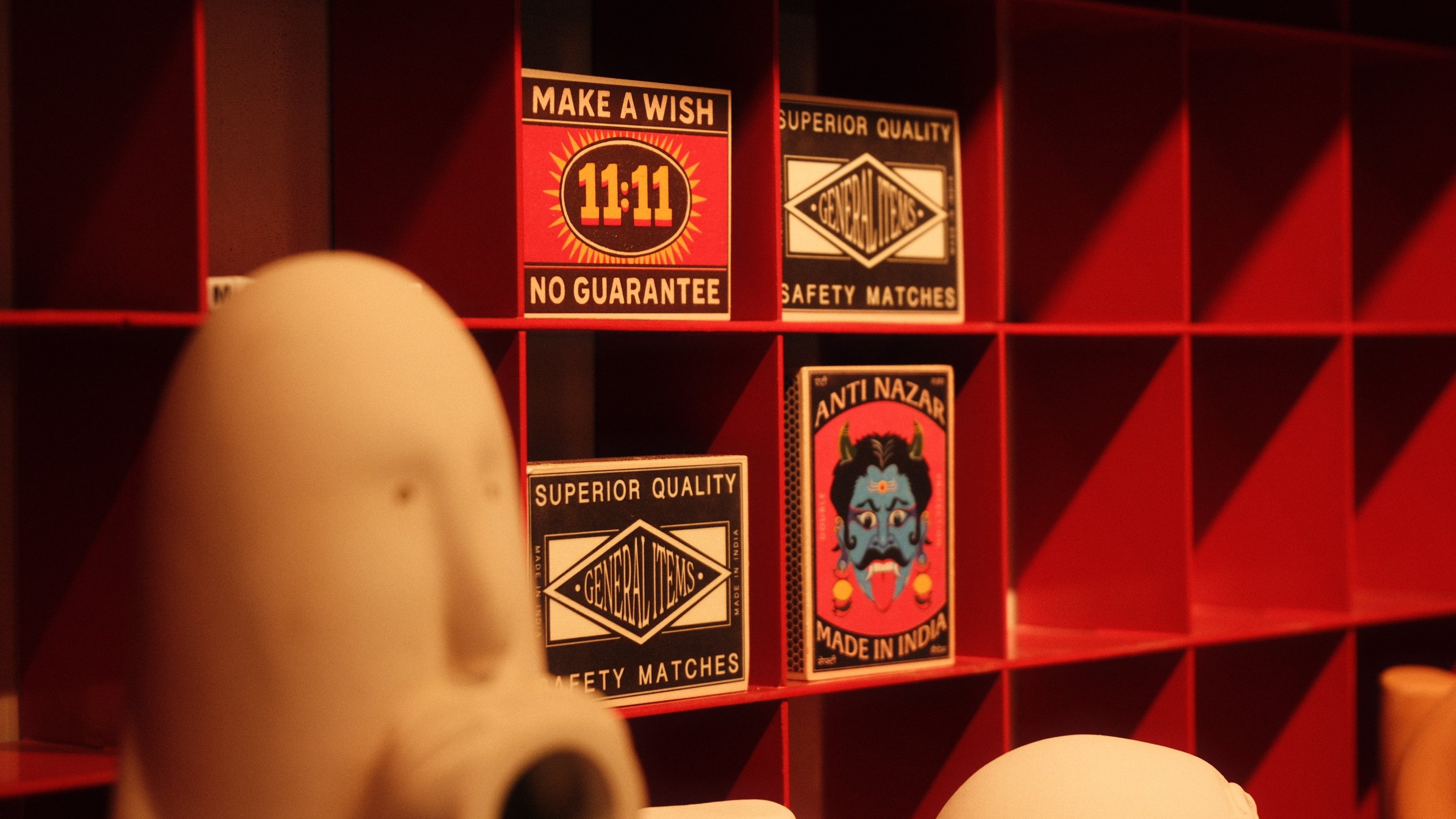 Vintage matchbox labels on a red grid shelf beside a white ceramic figure