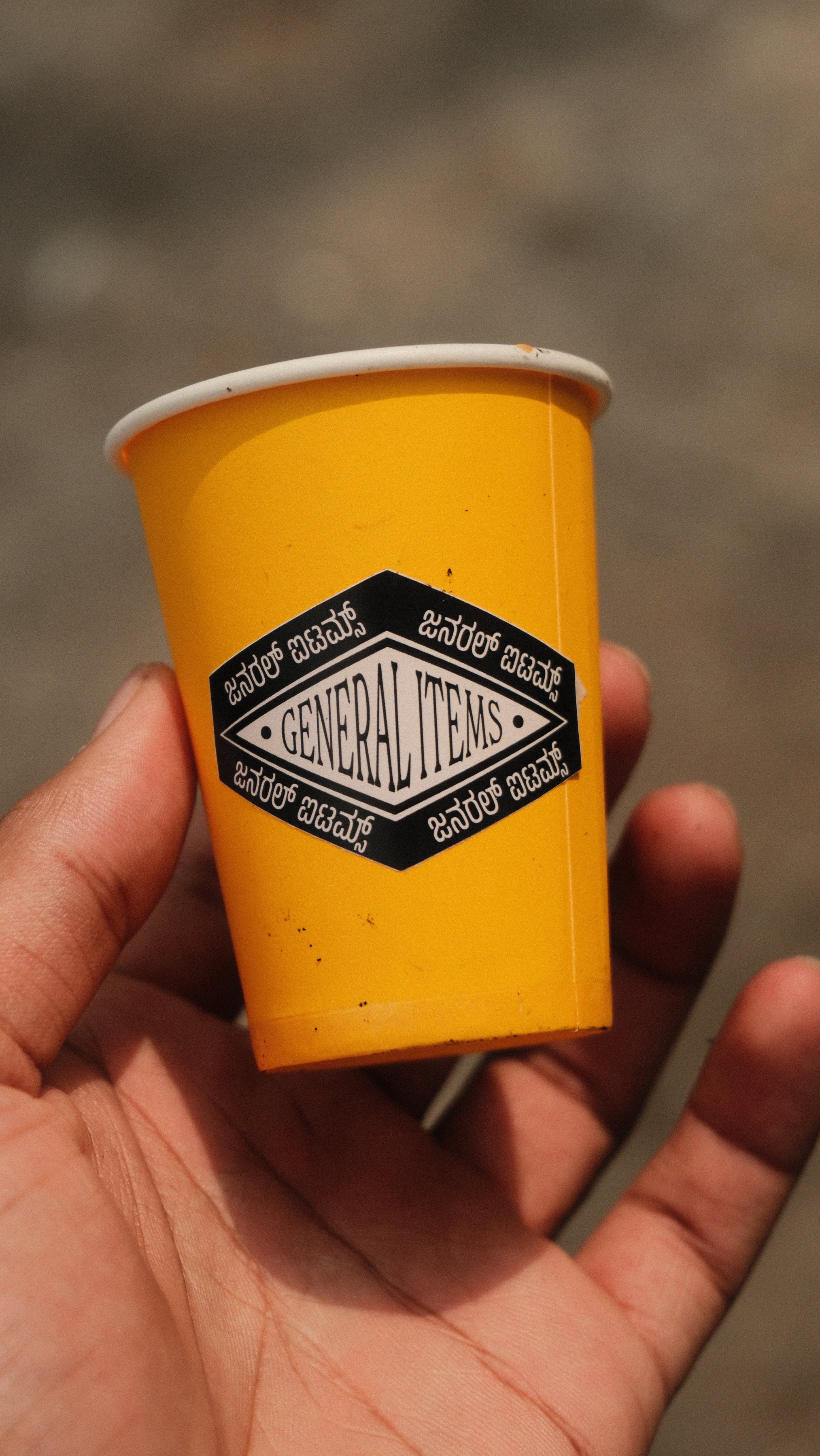 A hand holding a yellow paper cup printed with the shop logo