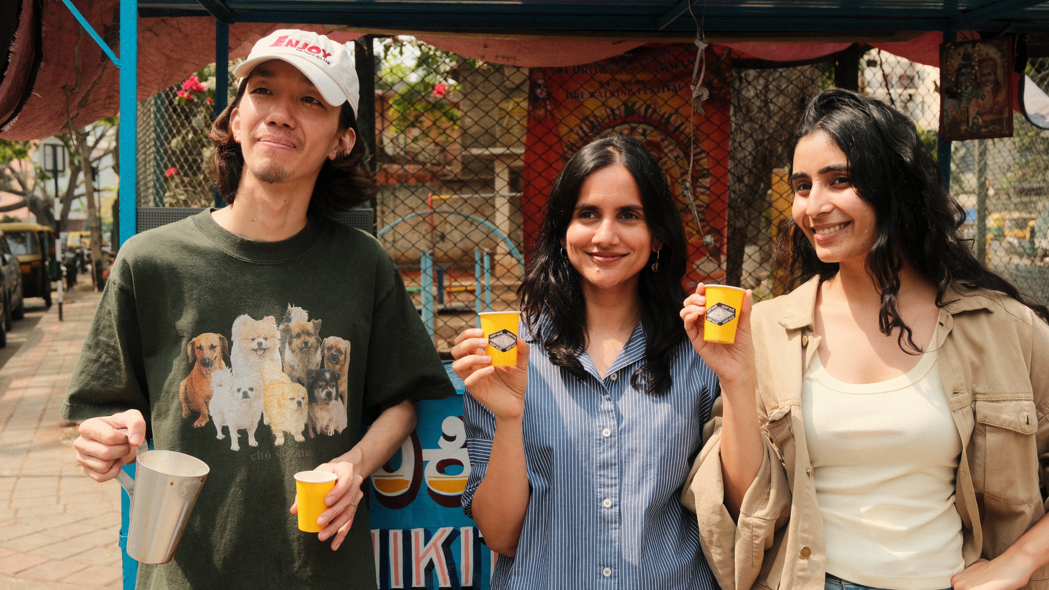 Three friends smiling with yellow branded cups at a street stall