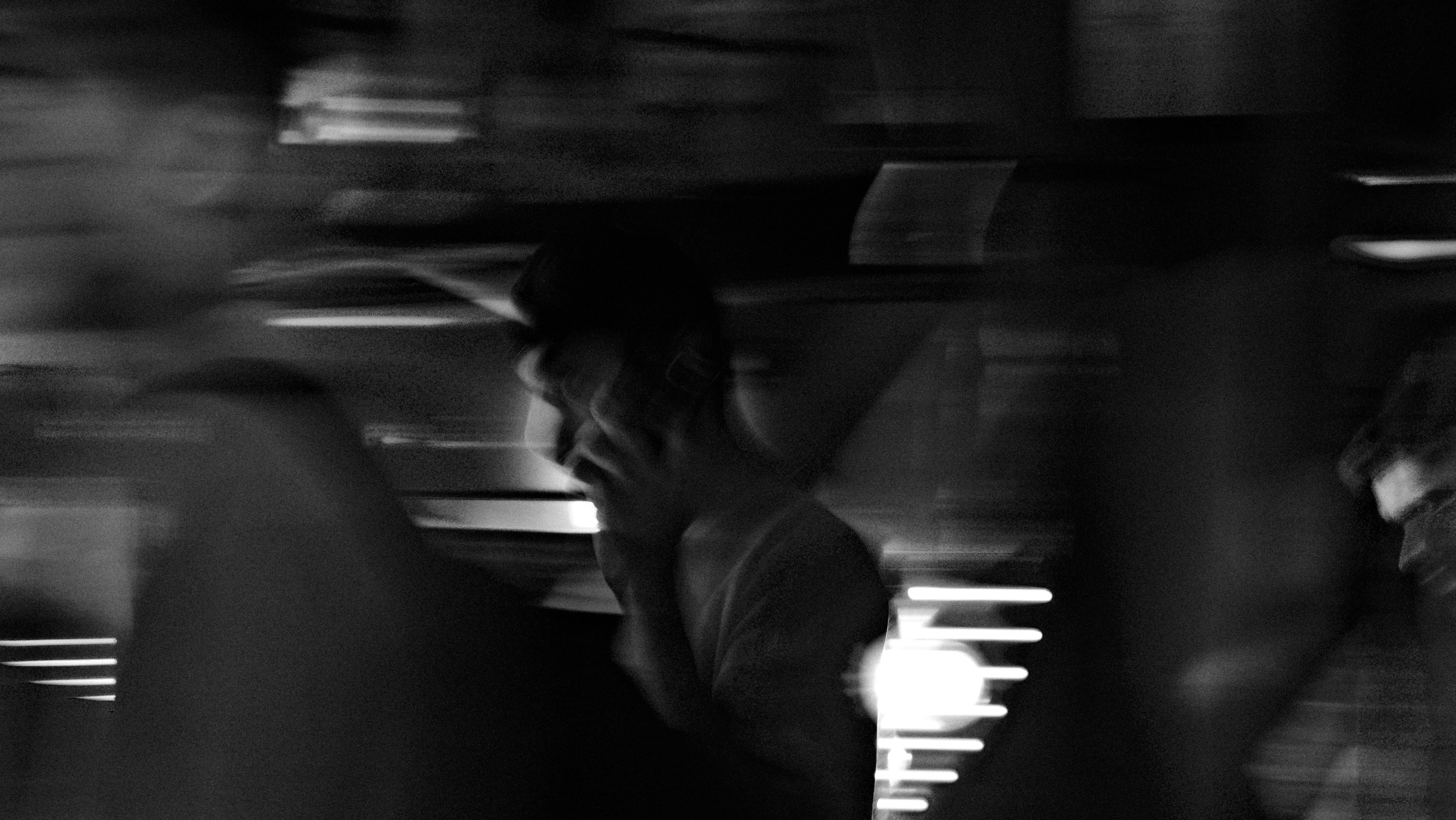 A blurred figure in a dark room lit by window light, in black and white