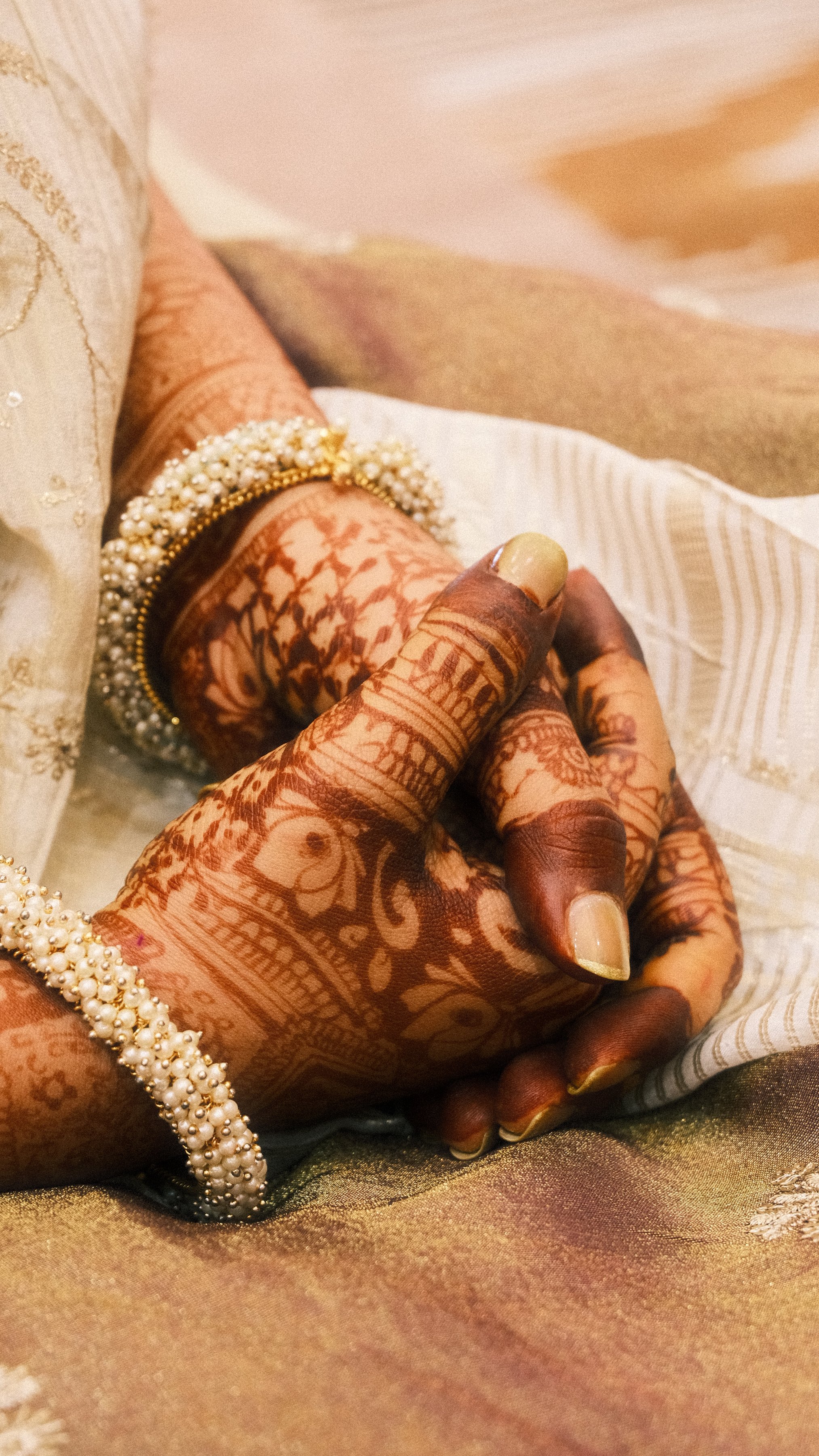 Hennaed hands with pearl bangles resting in a lap
