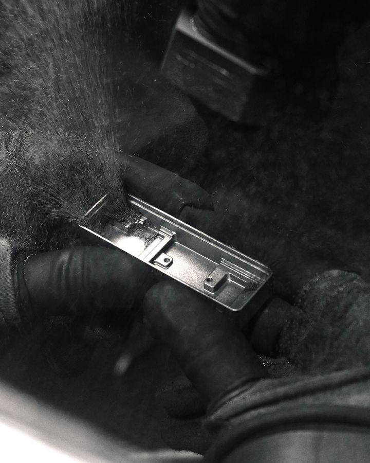 Hands in work gloves polishing a small metal component, dust in the air, in black and white
