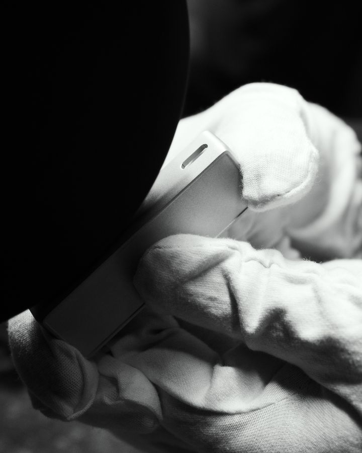 Gloved hands holding a finished metal part against a dark background, in black and white