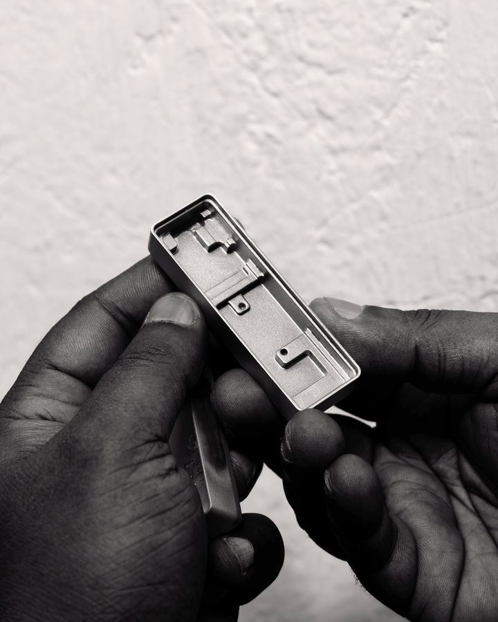 Hands holding a machined aluminium housing against a rough white wall, in black and white