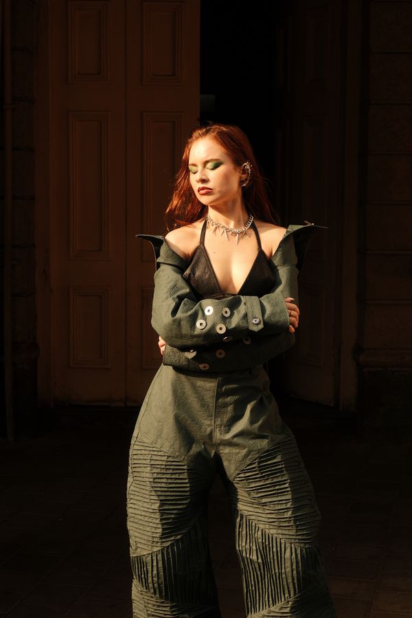 A model with arms crossed standing in a dark wooden doorway