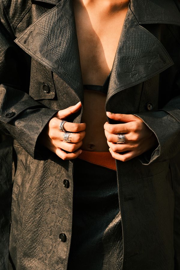 Hands with silver rings holding open a dark leather trench coat