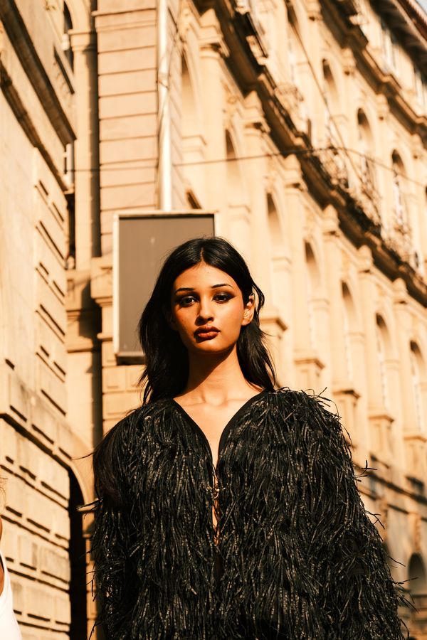 A model in a black feather jacket in front of a heritage facade