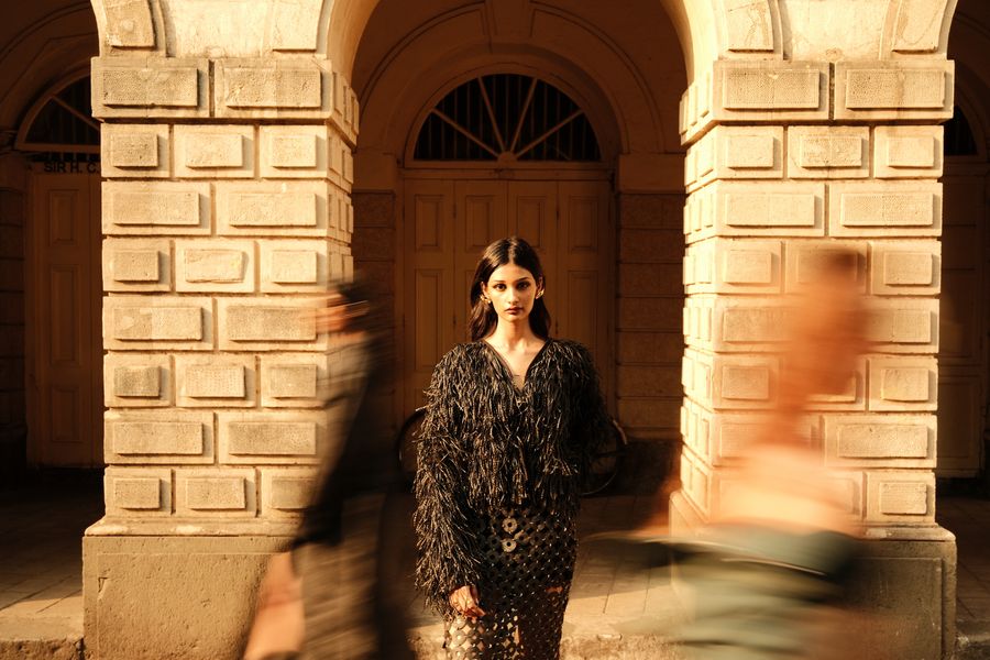 A model standing still in an arcade as blurred figures pass