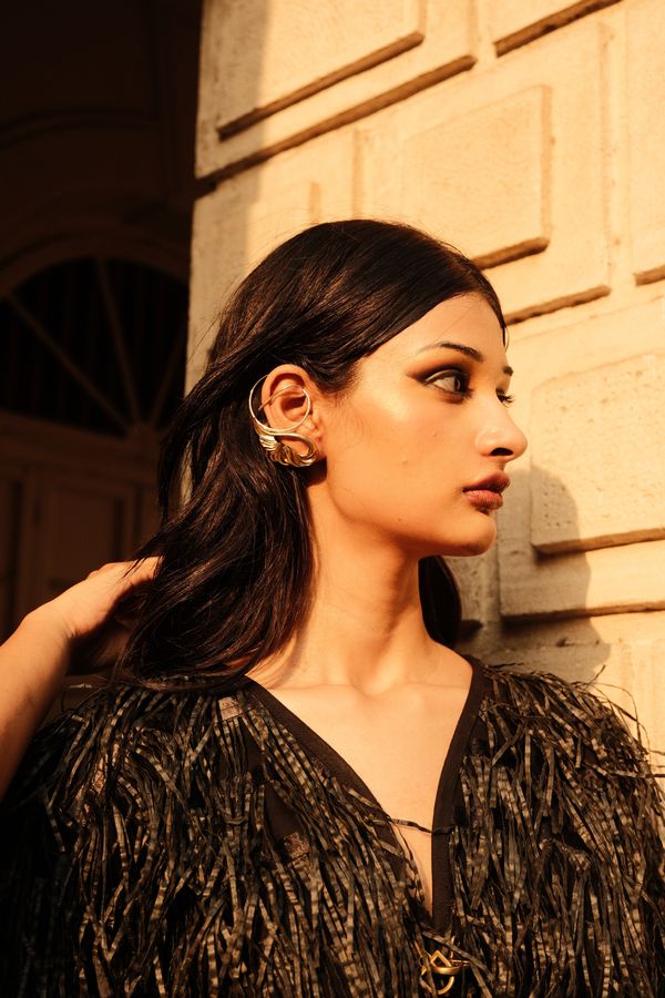 A model in a feather jacket with a gold ear cuff, a hand in their hair
