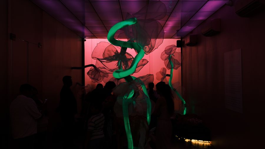 Visitors moving through the dark room beneath the green neon sculpture