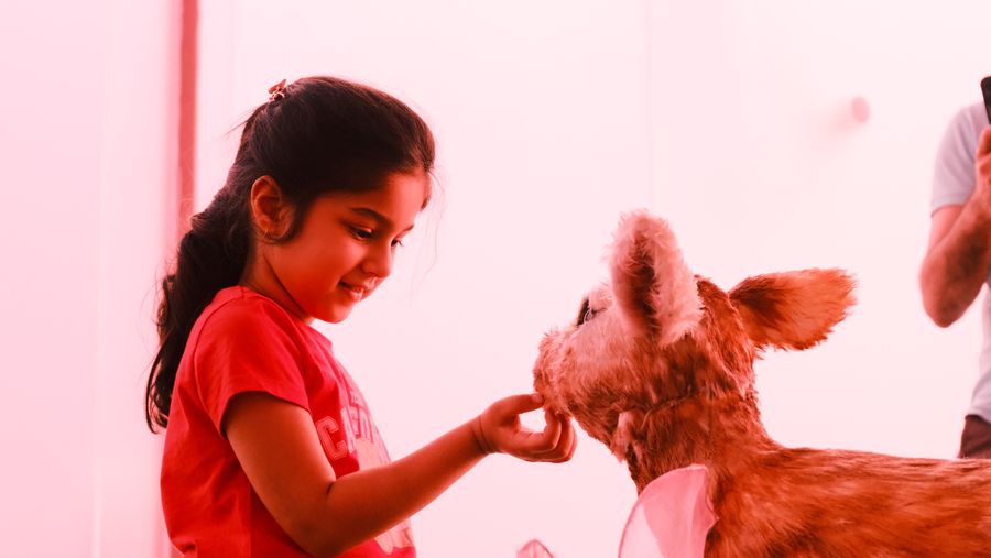 A girl in red holding her hand out to a fawn sculpture