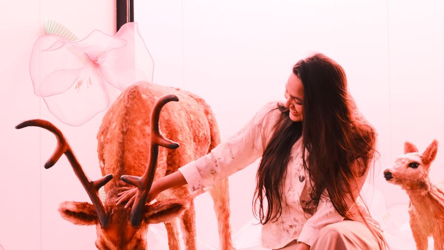 A woman smiling as she reaches toward a stag sculpture, a fawn beside her