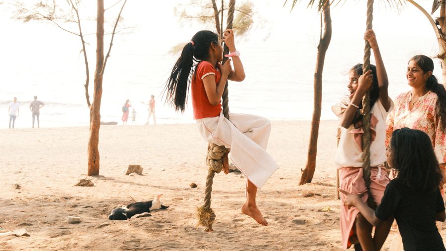 Young women playing on rope swings tied to trees on a beach