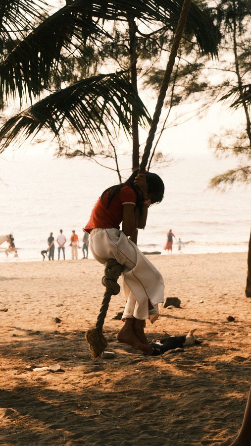 A girl in red swinging on a rope against the bright sea
