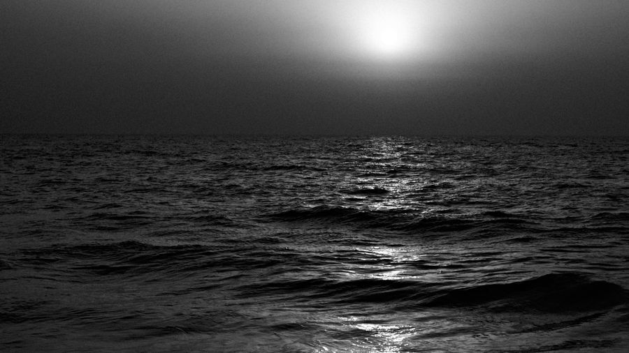 The evening sun breaking through haze over dark, rolling waves, in black and white