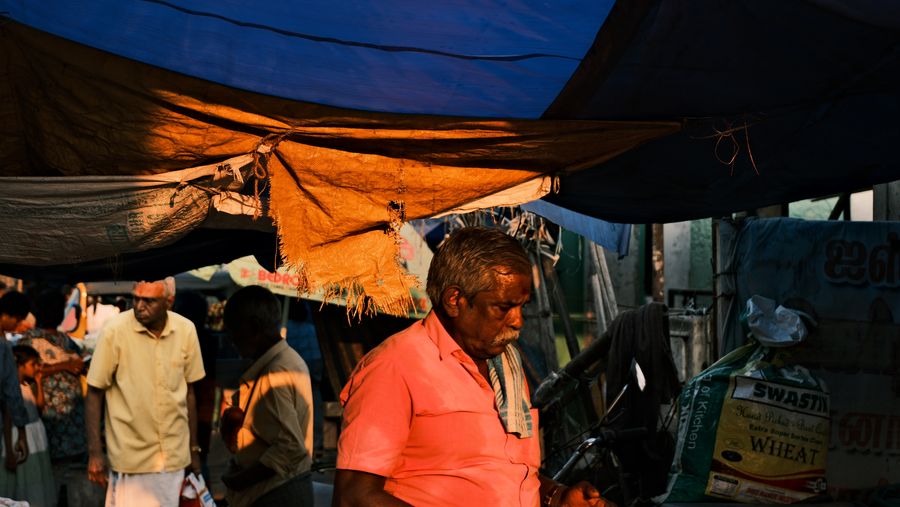 A man in an orange shirt walking beneath blue market tarps