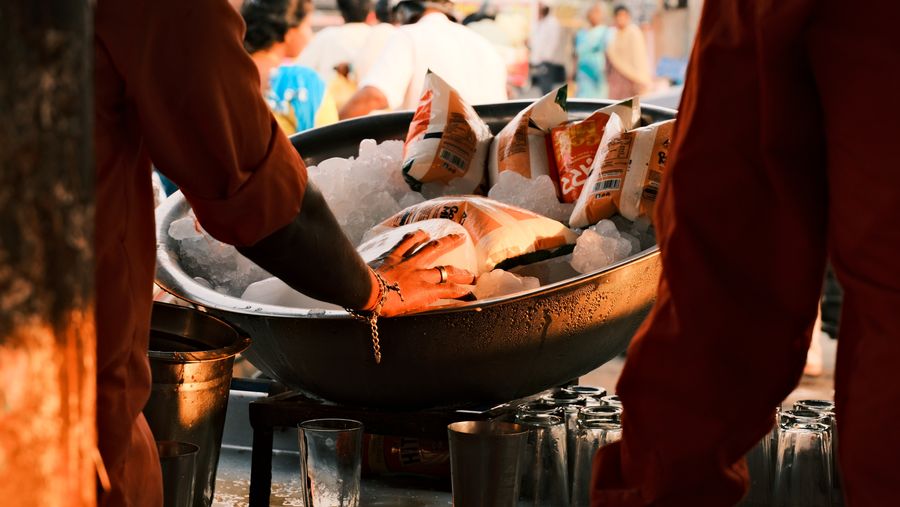 Hands reaching into a large bowl of ice and packets at a stall