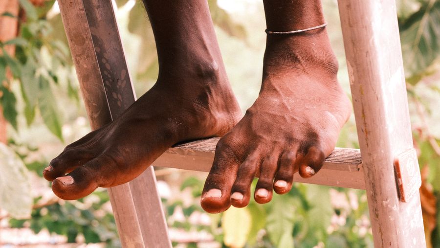 Bare feet resting on the rung of a wooden ladder