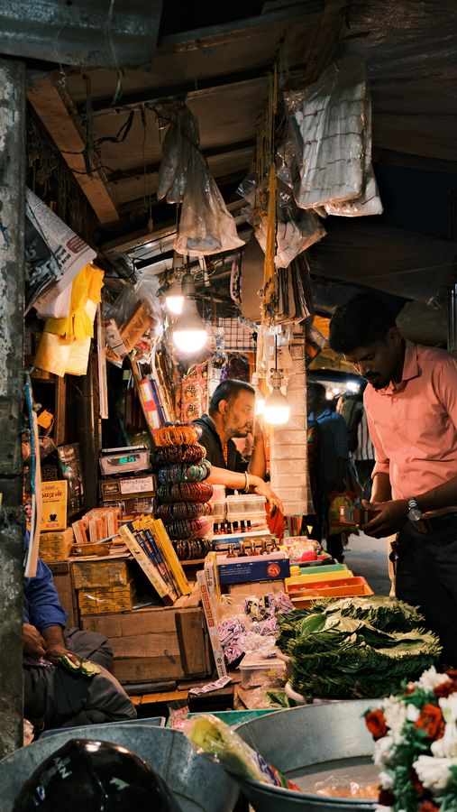 A market stall at night lit by bare bulbs, piled with goods