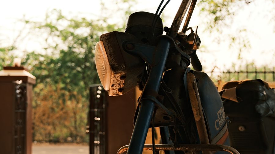 An old motorcycle parked by a gate, its headlight catching the afternoon sun