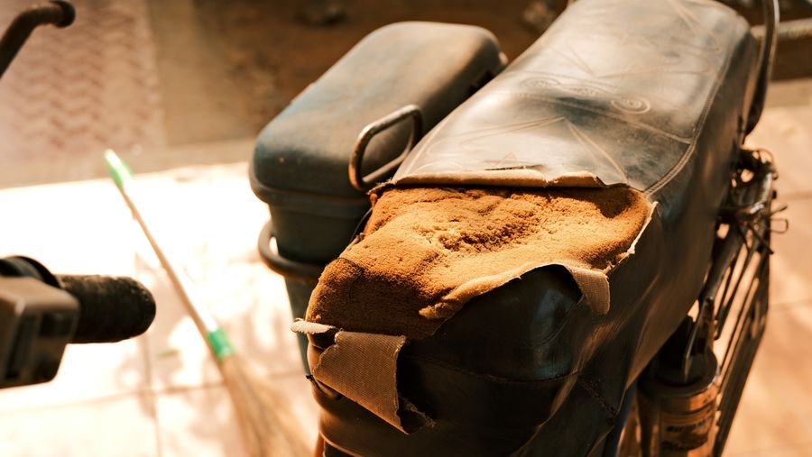 The torn seat of an old motorcycle patched with cloth, in warm afternoon light