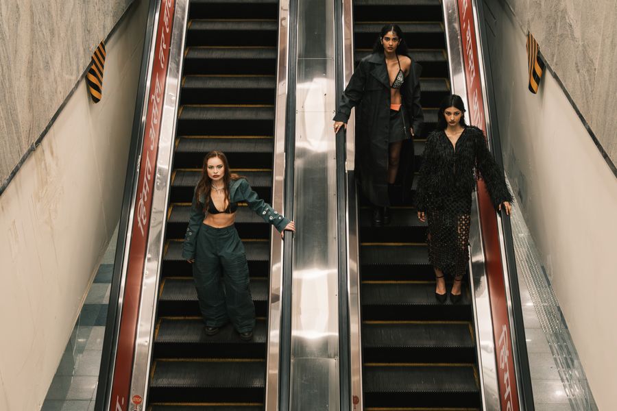 Three models in olive, leather and feathers on parallel escalators