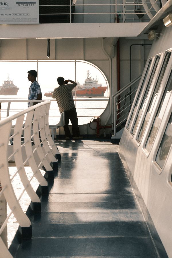Two people at the rail of a ferry looking out at ships