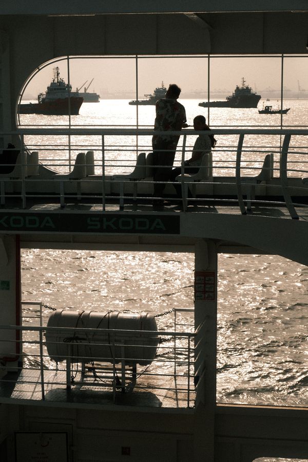 Figures on the upper deck of a ferry against a bright sea