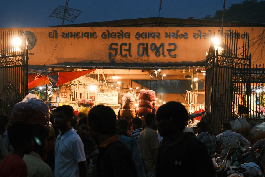Crowds under the lit gate of the wholesale flower market before dawn