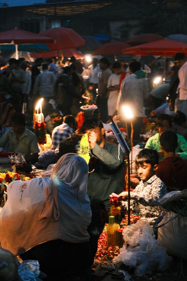 A lamp-lit crowd of flower sellers and buyers under red umbrellas
