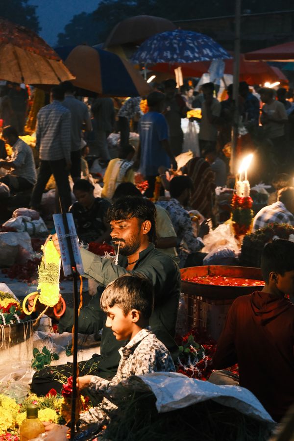 A boy at a flower stall lit by a hanging lamp