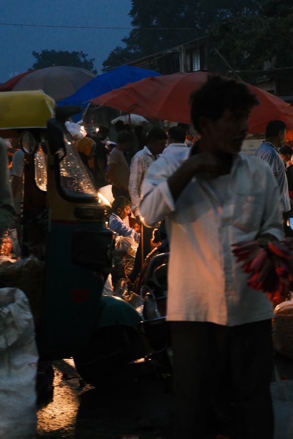 A man in a white shirt walking through the market under red and blue umbrellas