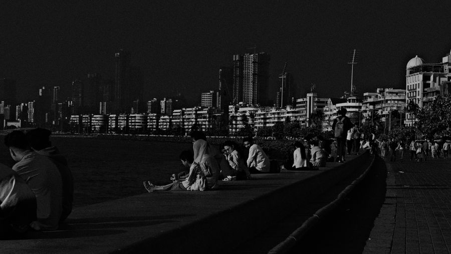 People sitting along the curving sea wall of Marine Drive, in black and white