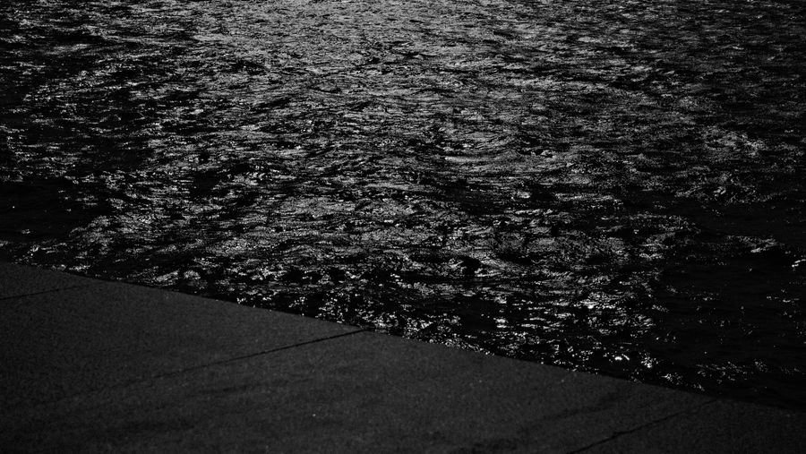 Dark water glittering beside an empty sea wall, in black and white