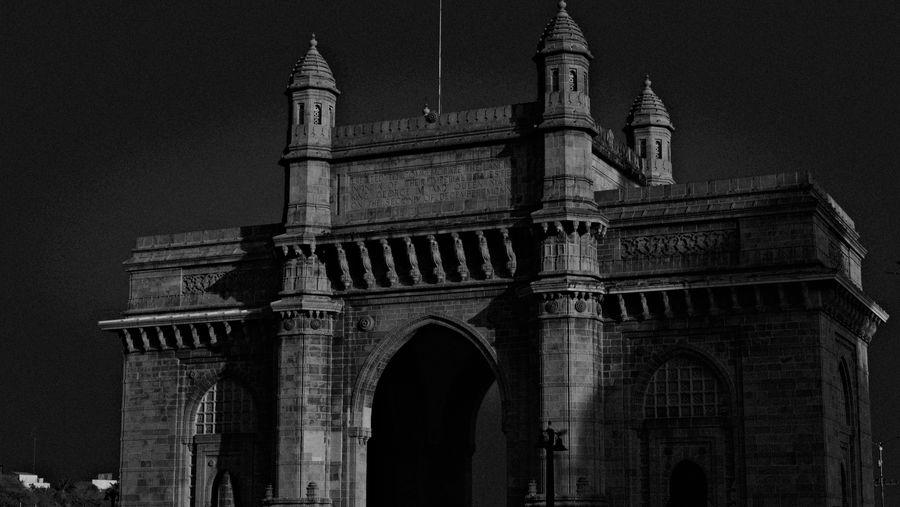 The carved stone Gateway of India against a dark sky, in black and white